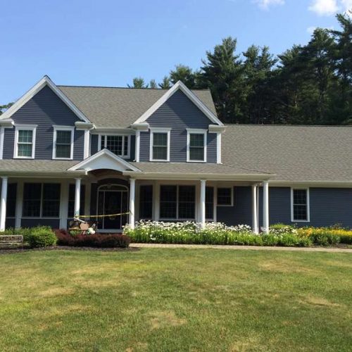 A large colonial house professionally painted blue with white accents, painted by Liberty Painting and Siding.