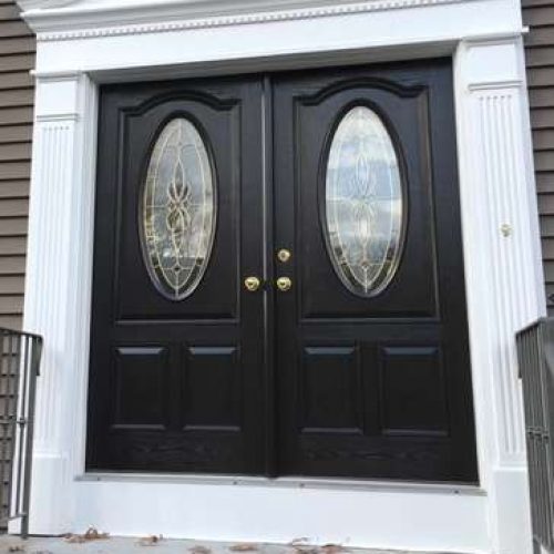 A completed front door replacement project featuring double black doors with golden knobs and oval windows