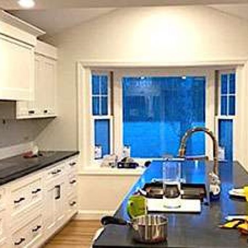 This freshly completed kitchen remodeling project has a modern and minimalist look, with white walls and cabinets accented by black counters and hardware.