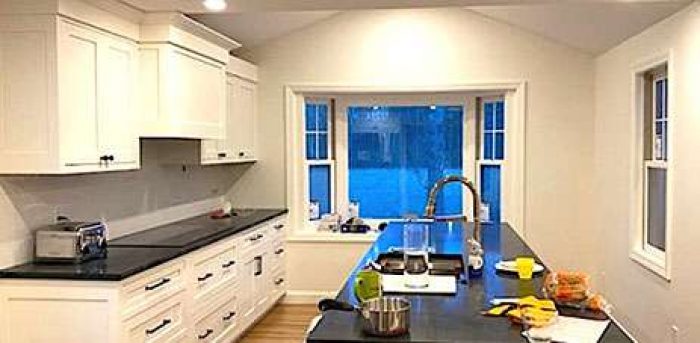 This freshly completed kitchen remodeling project has a modern and minimalist look, with white walls and cabinets accented by black counters and hardware.