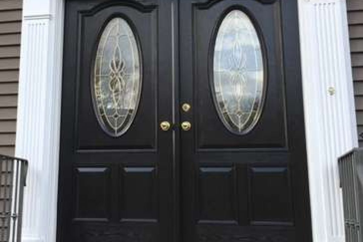 A completed front door replacement project featuring double black doors with golden knobs and oval windows