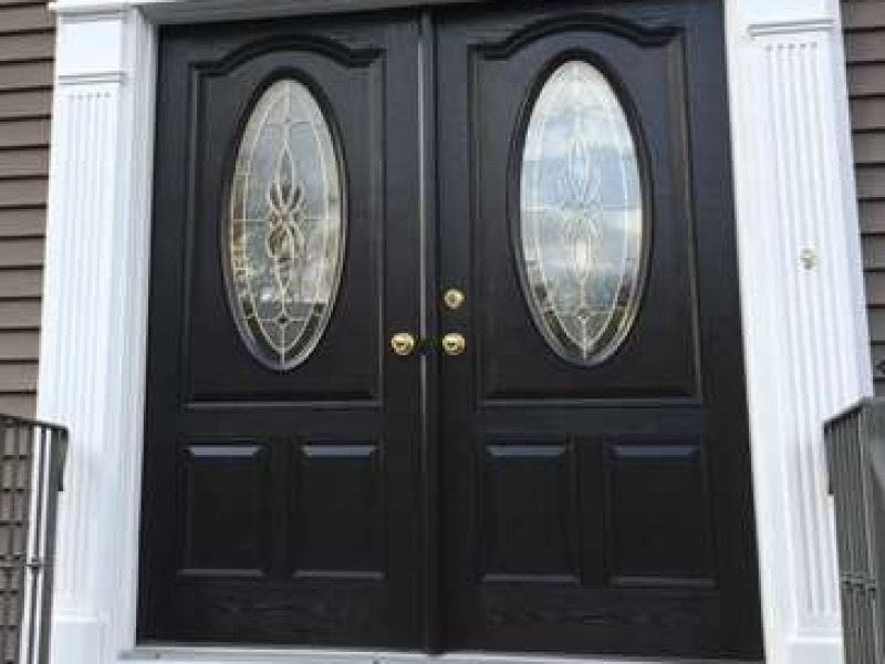 A completed front door replacement project featuring double black doors with golden knobs and oval windows