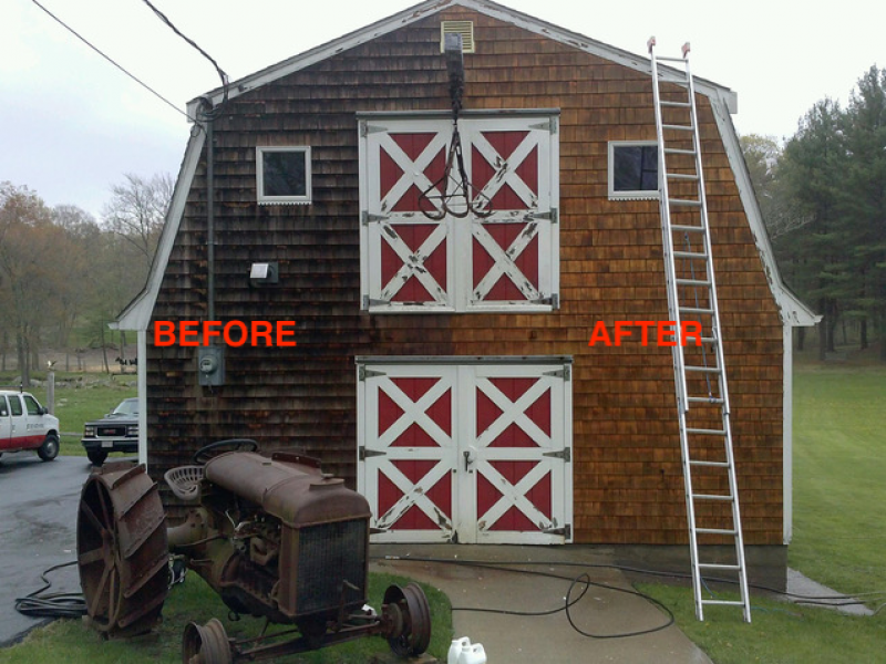 Photo of a Liberty Painting project mid-way to show how effective power-washing can be at cleaning on the exterior siding of a barn. One side is light red brown after washing while the other is dark with soot and debris.